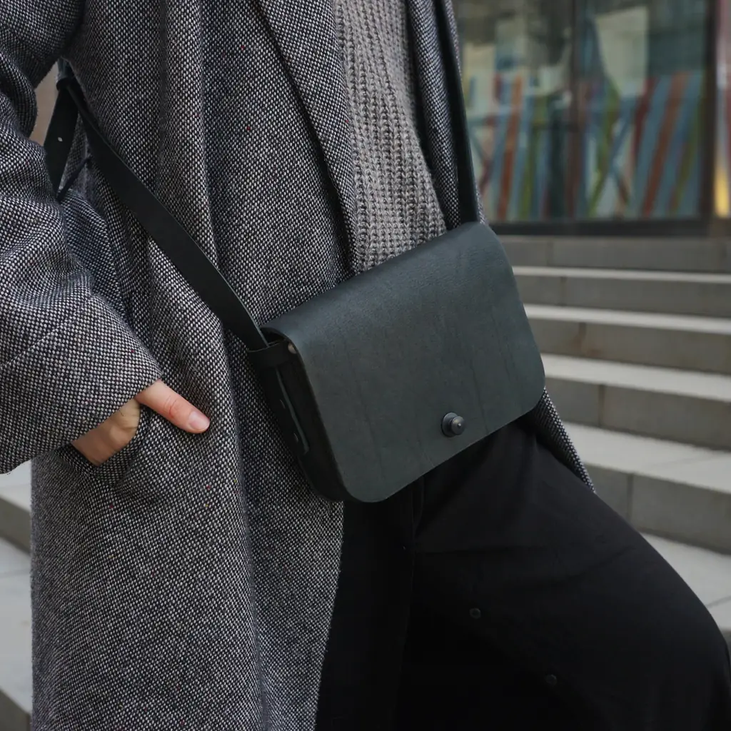 A nylon crossbody travel bag strapped over a puffer coat, seen from behind