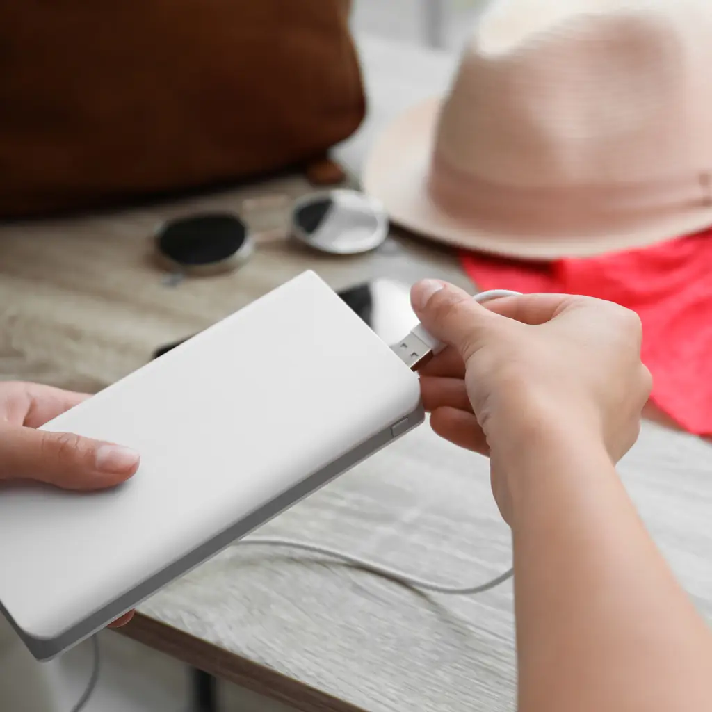 A small power bank charging a phone on an airplane tray table, kept in plain view