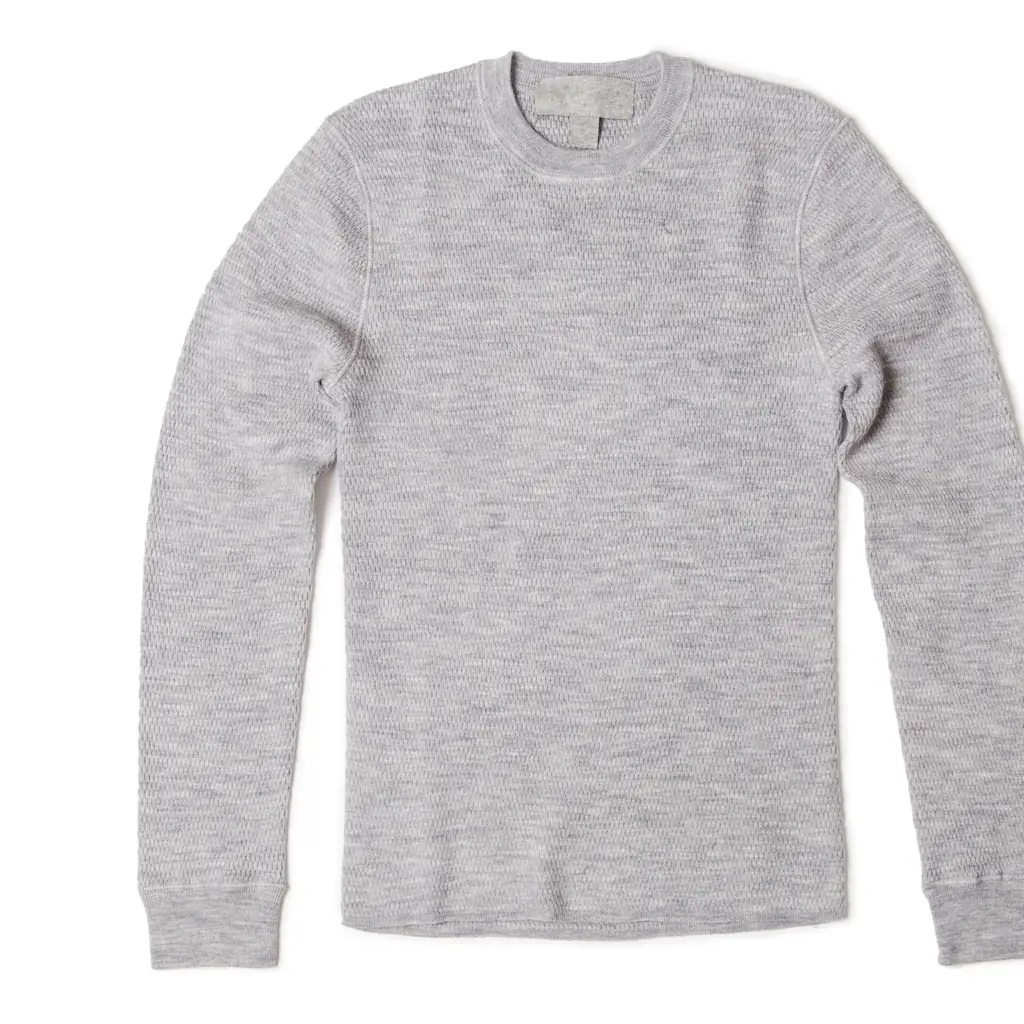 Two thin folded merino base-layer tops beside a bulky sweater on a bed