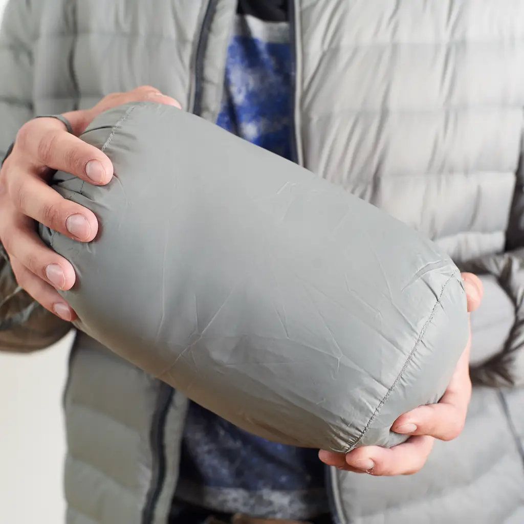 A lightweight down jacket being stuffed into its compression sack next to a water bottle for scale