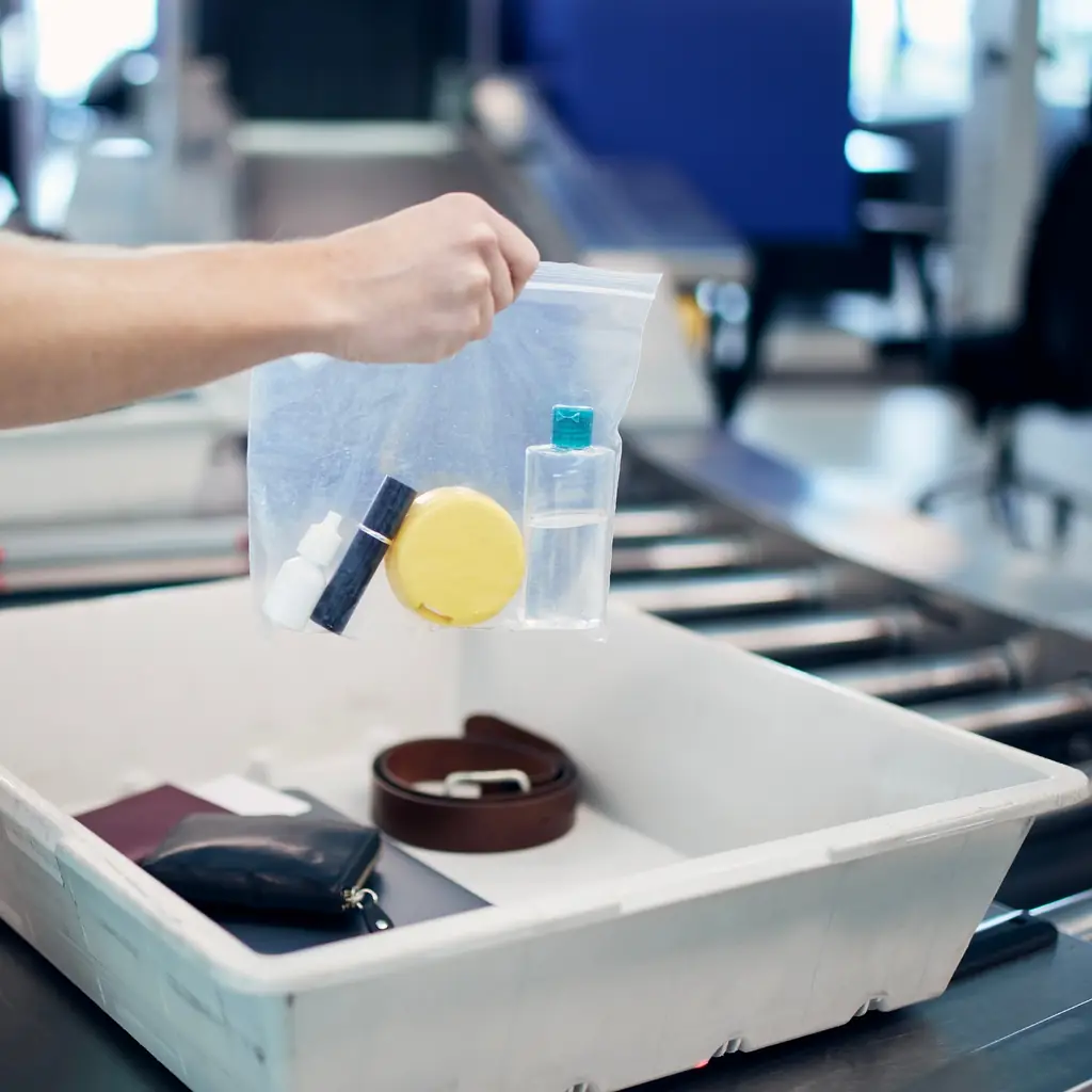A clear quart bag of small travel bottles going into an airport security tray