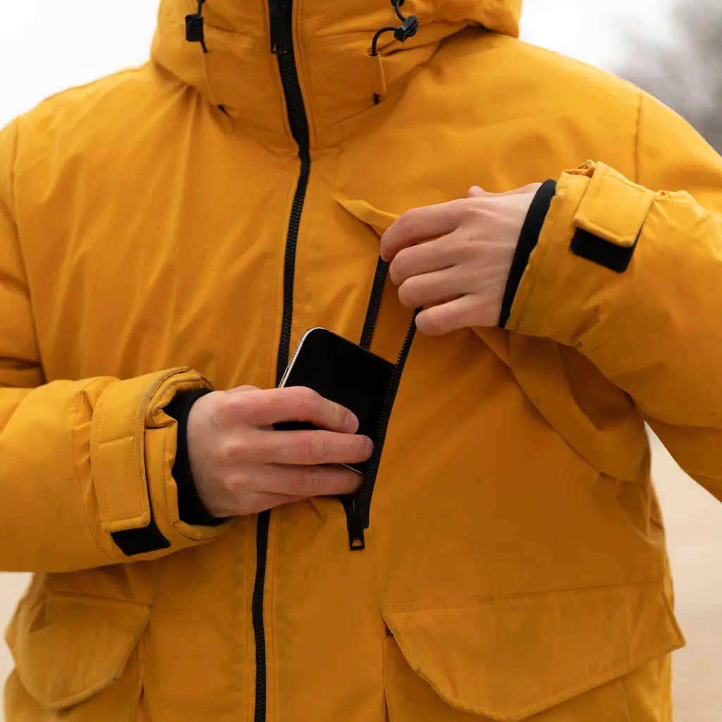 Hands slipping a smartphone into the chest pocket of a yellow winter parka