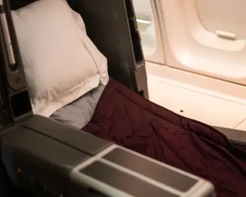 A business class seat made up as a flat bed with a pillow and duvet in a dimmed long-haul cabin