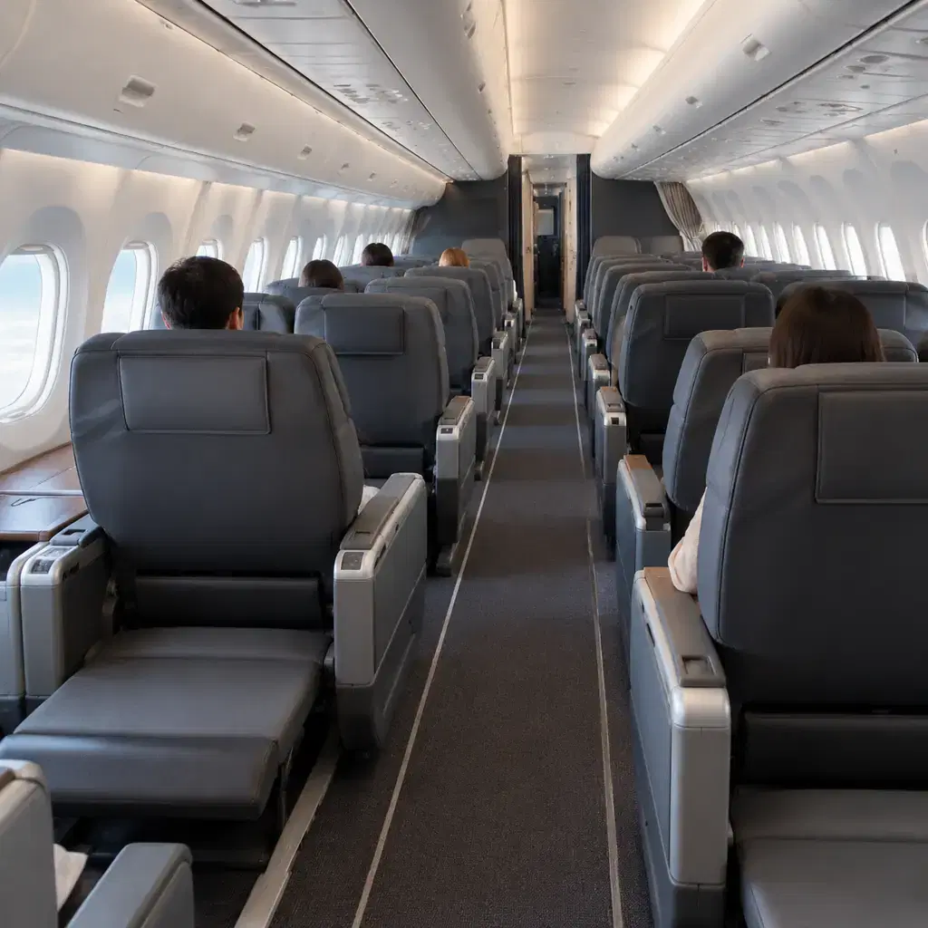 A premium economy cabin with rows of wide seats and leg rests seen from the aisle