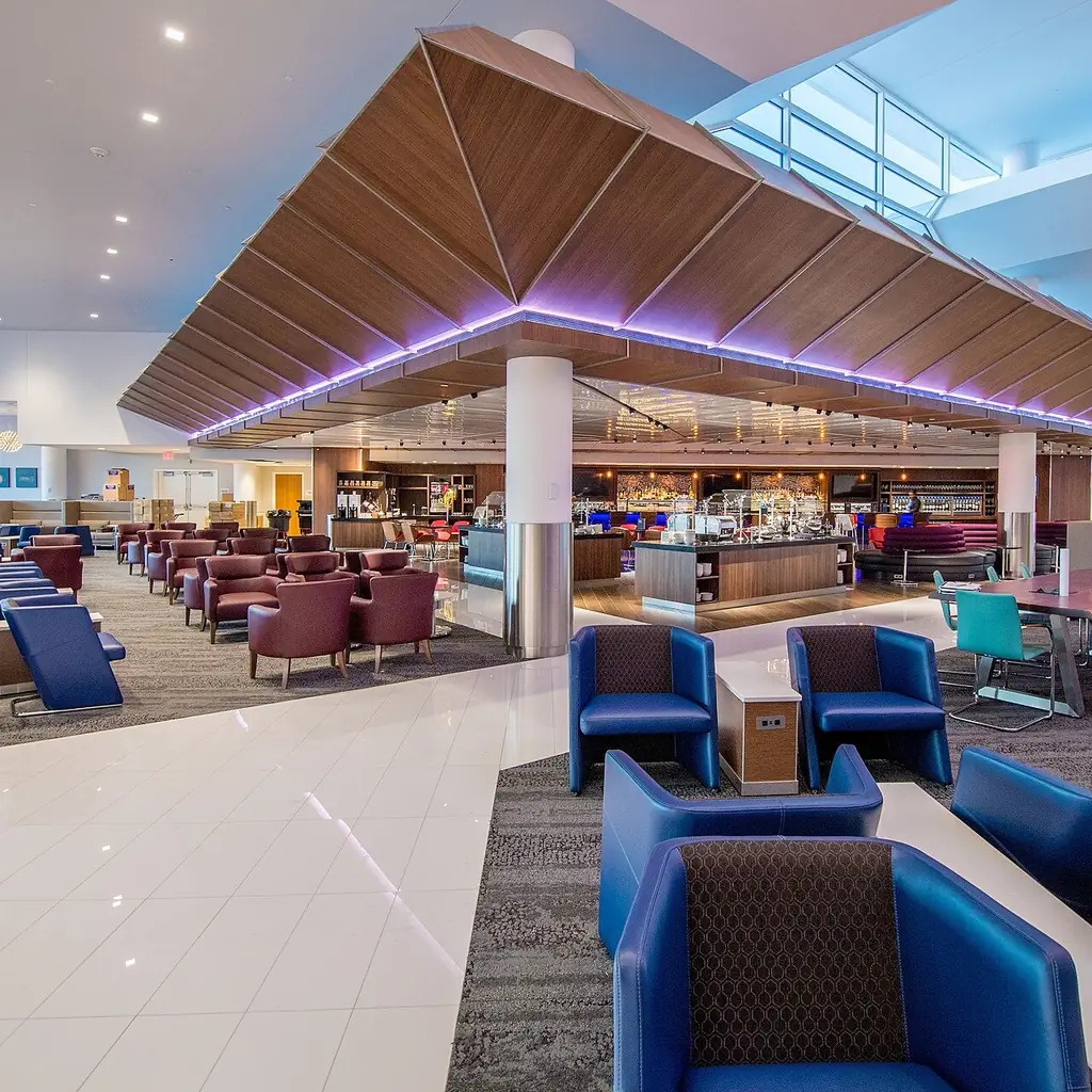 The interior of a Delta Sky Club airport lounge with armchairs and a bar