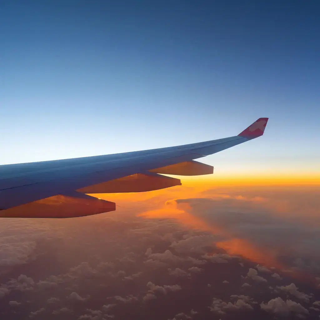 An airliner wing over a sea of clouds at sunset seen from a window seat on a long flight