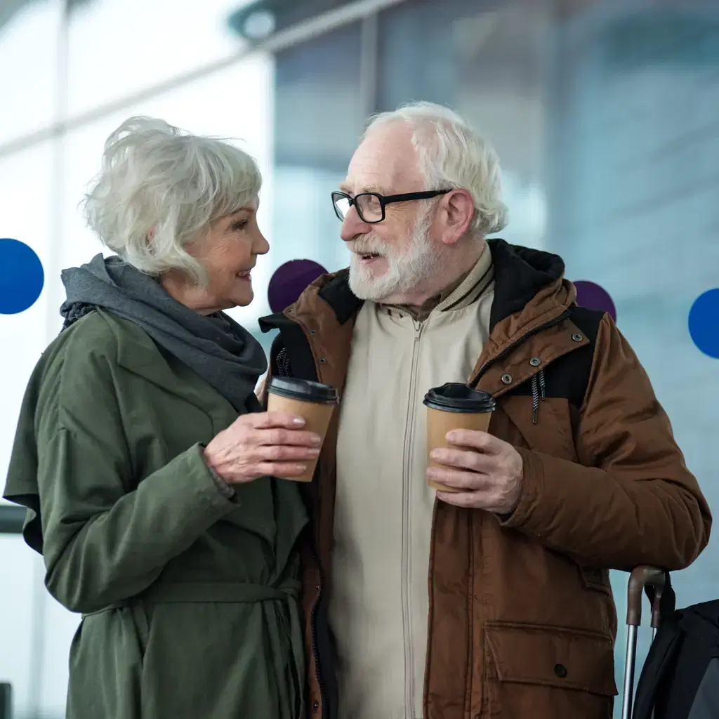 Two older travelers chatting over takeaway coffee in an airport terminal