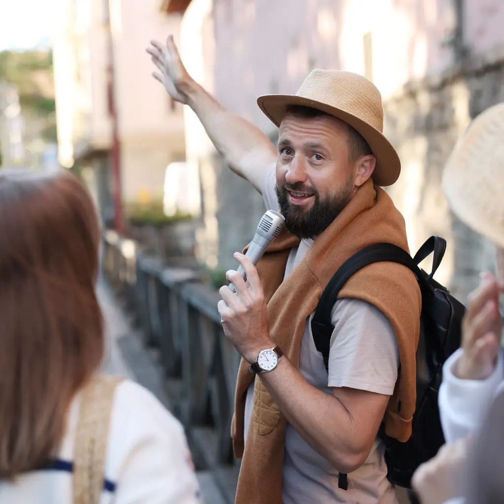 A tour guide with a microphone speaking to a group of tourists on a European city street, illustrating group size and who you are traveling with.