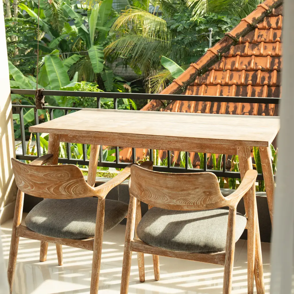 A cozy hotel balcony with a wooden table overlooking tropical garden landscaping, illustrating a garden-view room category.