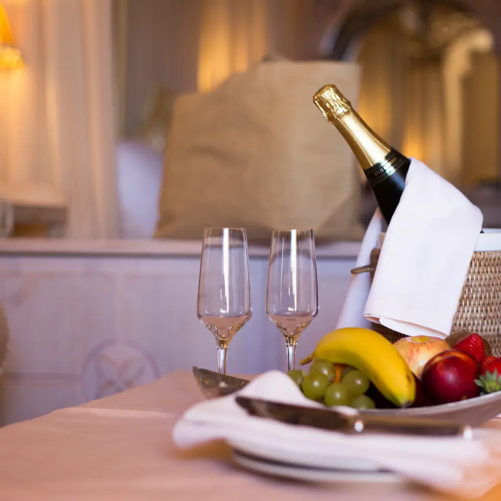Champagne, glasses, and a fruit basket set up in a hotel room, illustrating a welcome service included in the room rate.