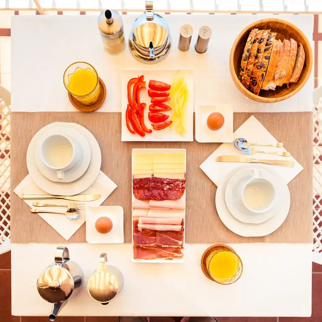 An overhead view of a continental breakfast table setting for two at a hotel, illustrating breakfast-inclusive rates.