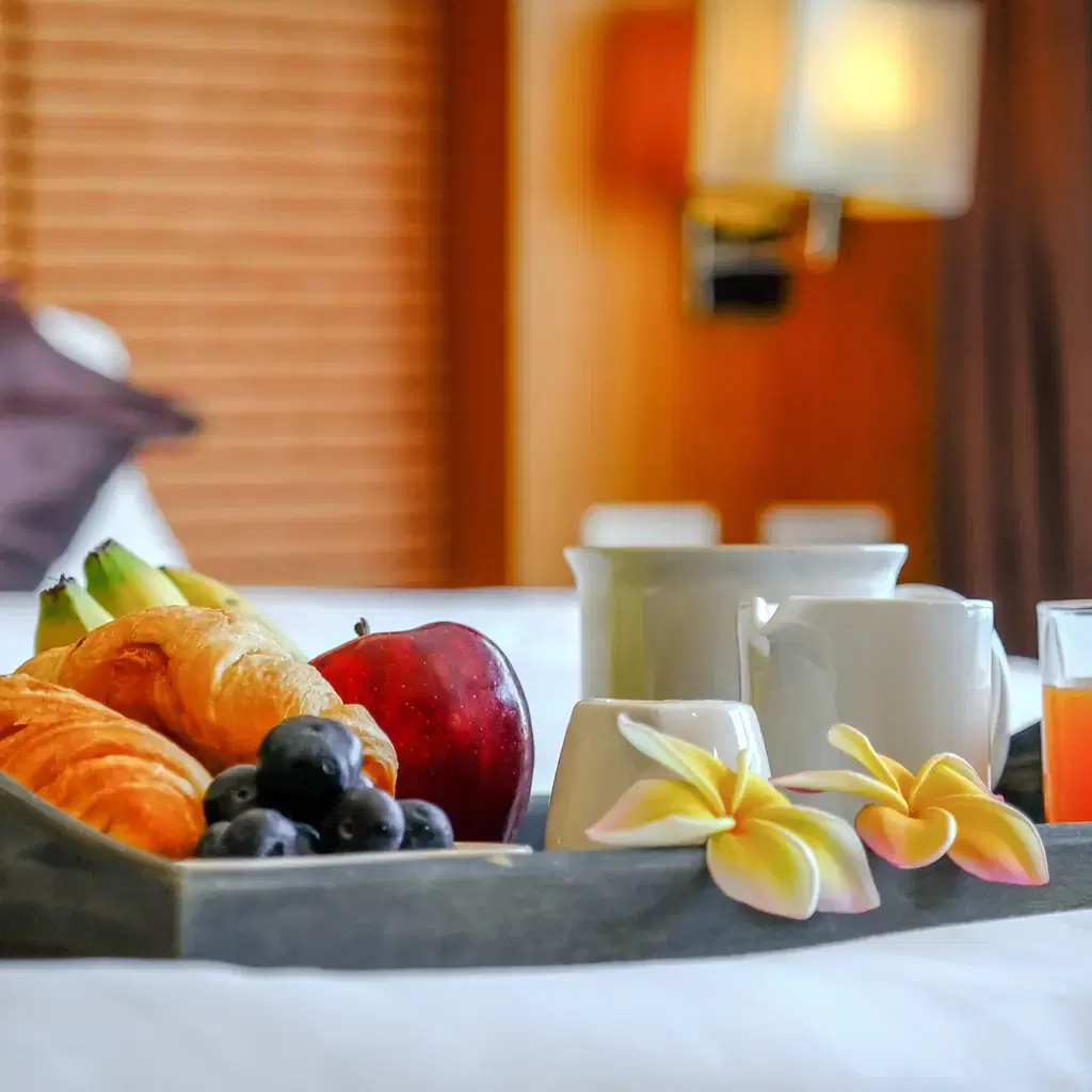 A breakfast tray with pastries and fruit set on a hotel bed, illustrating breakfast arriving as a status perk.