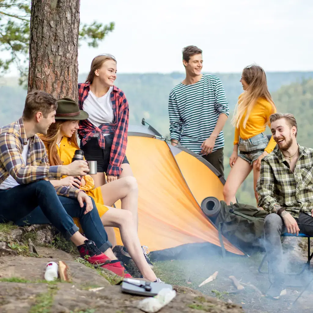 A group of young travelers camping and socializing outdoors, illustrating budget-tier operators trading inclusions for a lower price and younger crowd.