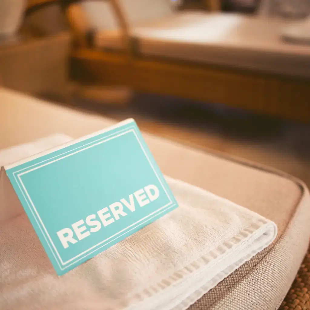 A reserved sign on a towel atop a resort sun lounger, illustrating exclusive pool or beach access bundled into a club tier.