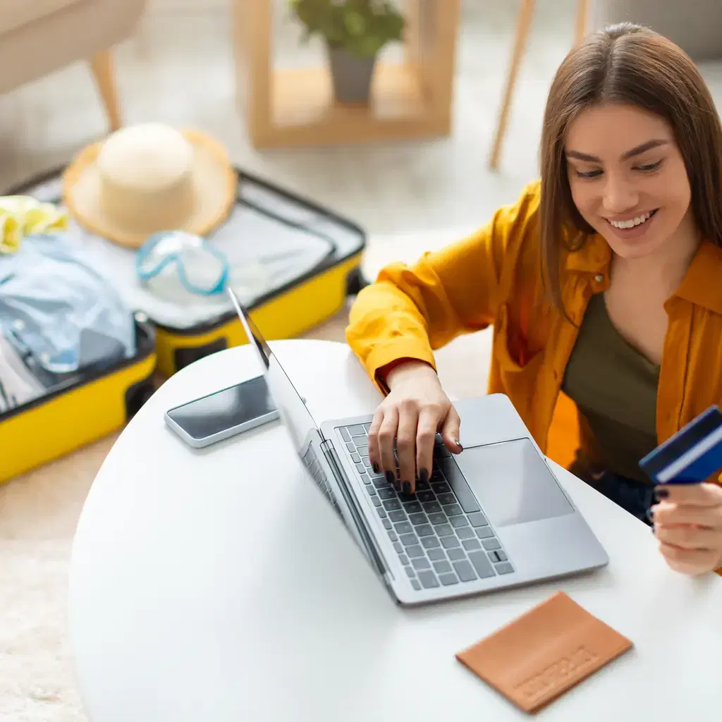 A traveler booking a flight online with a credit card next to a packed suitcase, illustrating buying an upgraded fare class outright.