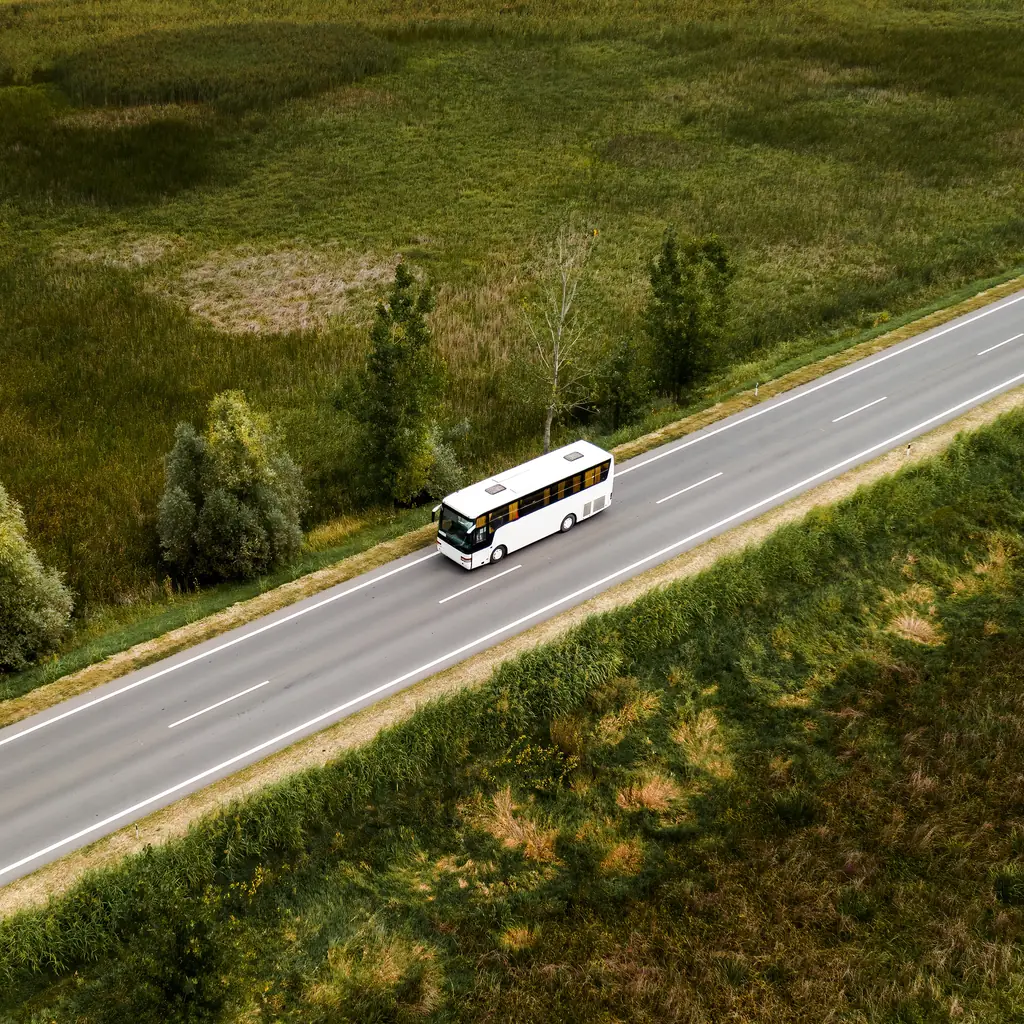 An aerial view of a tour bus driving along a road through green countryside, illustrating how coach and small-group models handle the drive between cities.