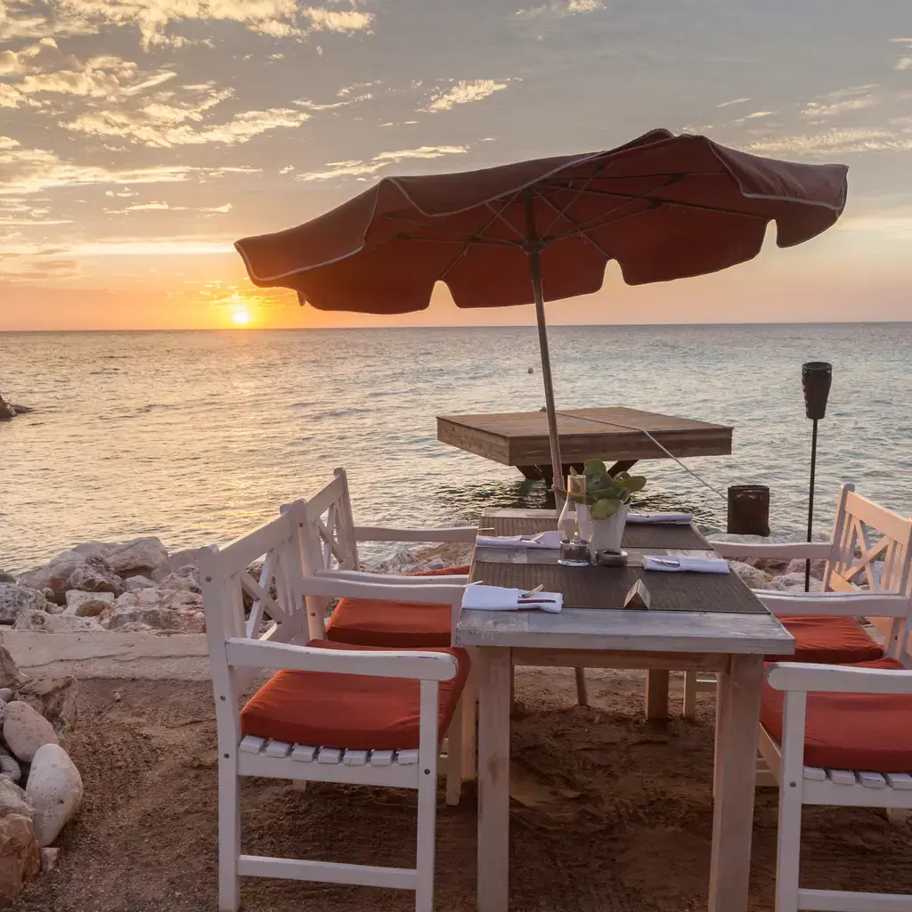 A dining table set up beside the ocean at sunset, illustrating a dedicated a la carte restaurant tied to a resort upgrade.