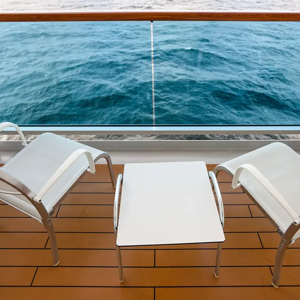 Two empty chairs and a table on a cruise ship balcony, illustrating the cruise-side version of the same room-category upgrade logic.
