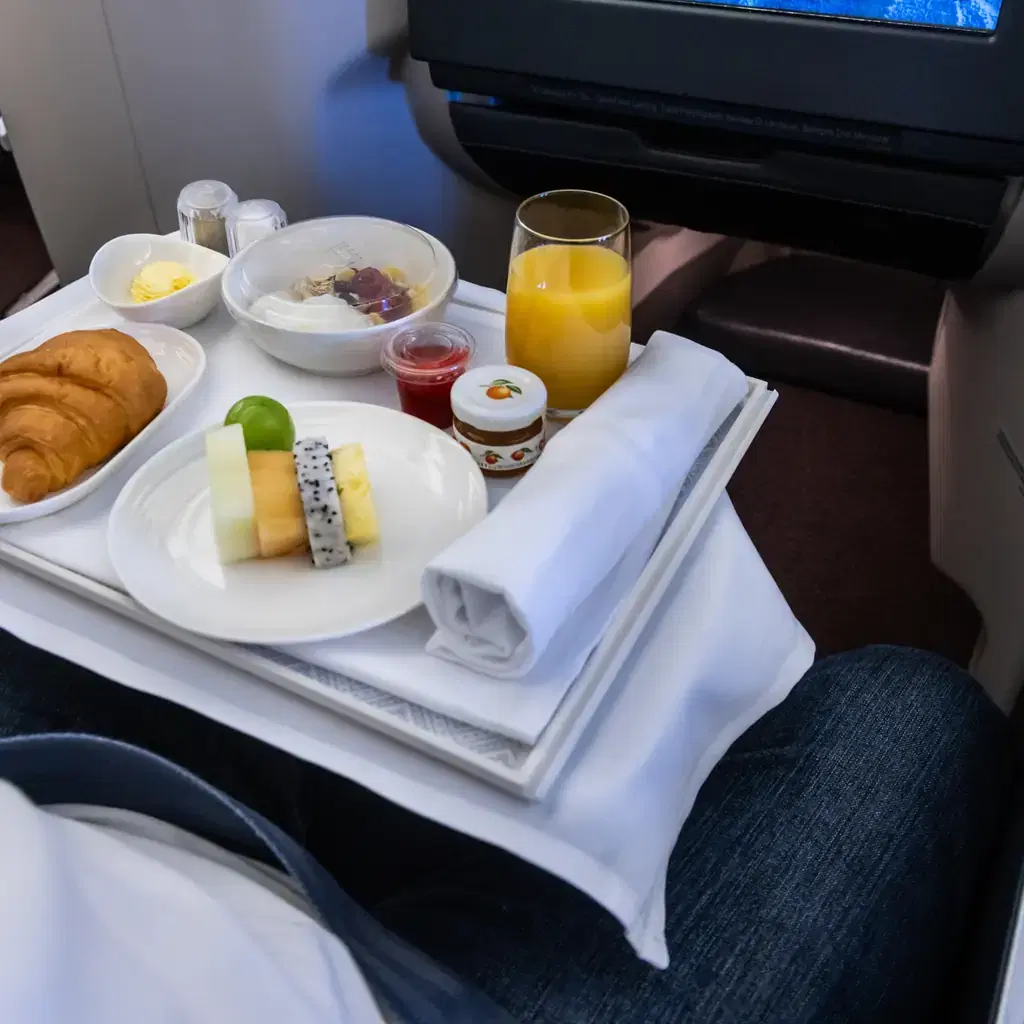An in-flight breakfast tray with croissant and fruit, illustrating how onboard service varies by carrier and cabin.