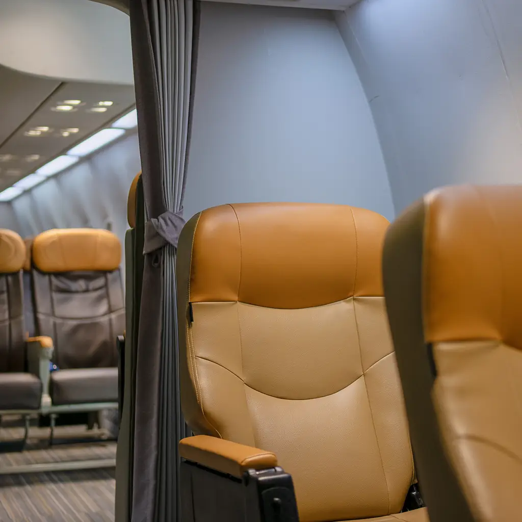 Wide orange leather recliner seats inside a commercial airplane cabin, illustrating domestic first class as a wider seat rather than a lie-flat bed.