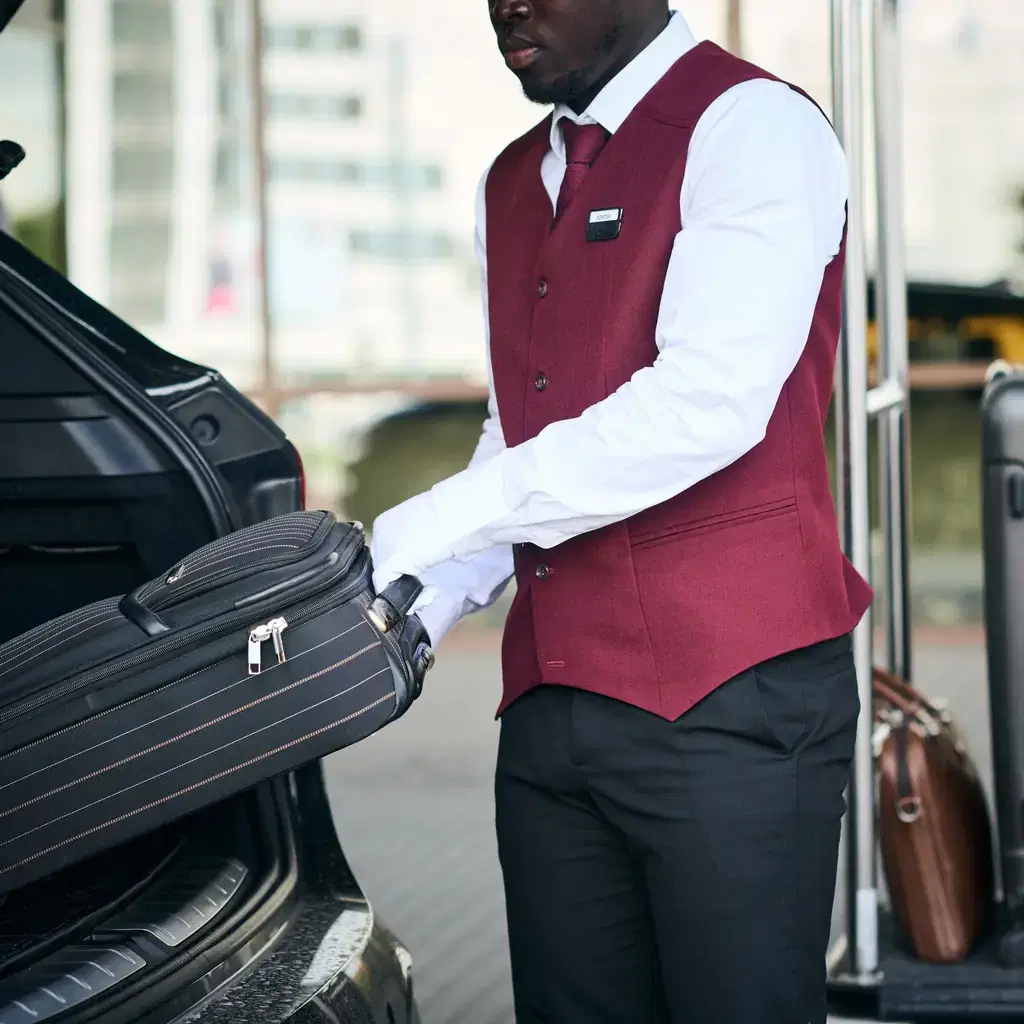 A uniformed doorman loading luggage into a car trunk, illustrating transfer quality starting before the tour itself begins.