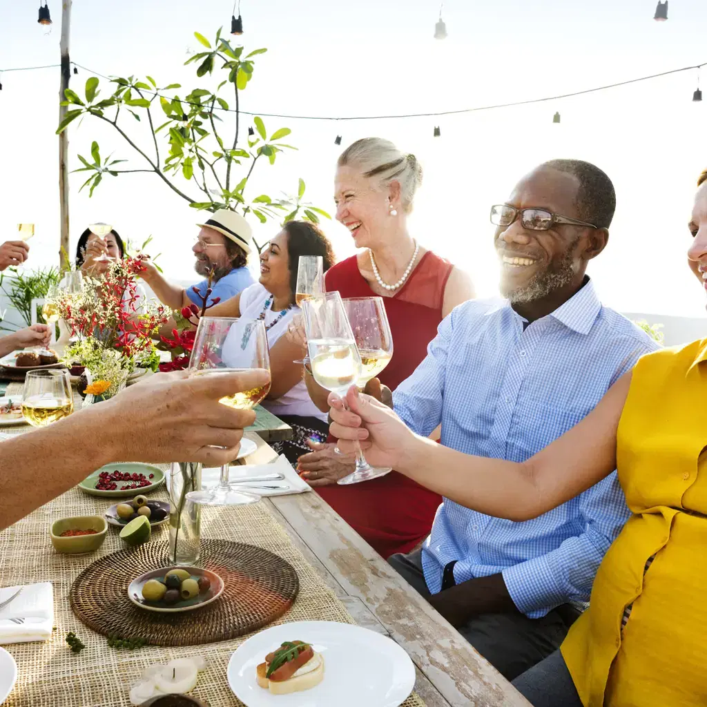 A group of travelers toasting with wine at an outdoor dinner table, illustrating meal inclusions varying by number and which meals are covered.