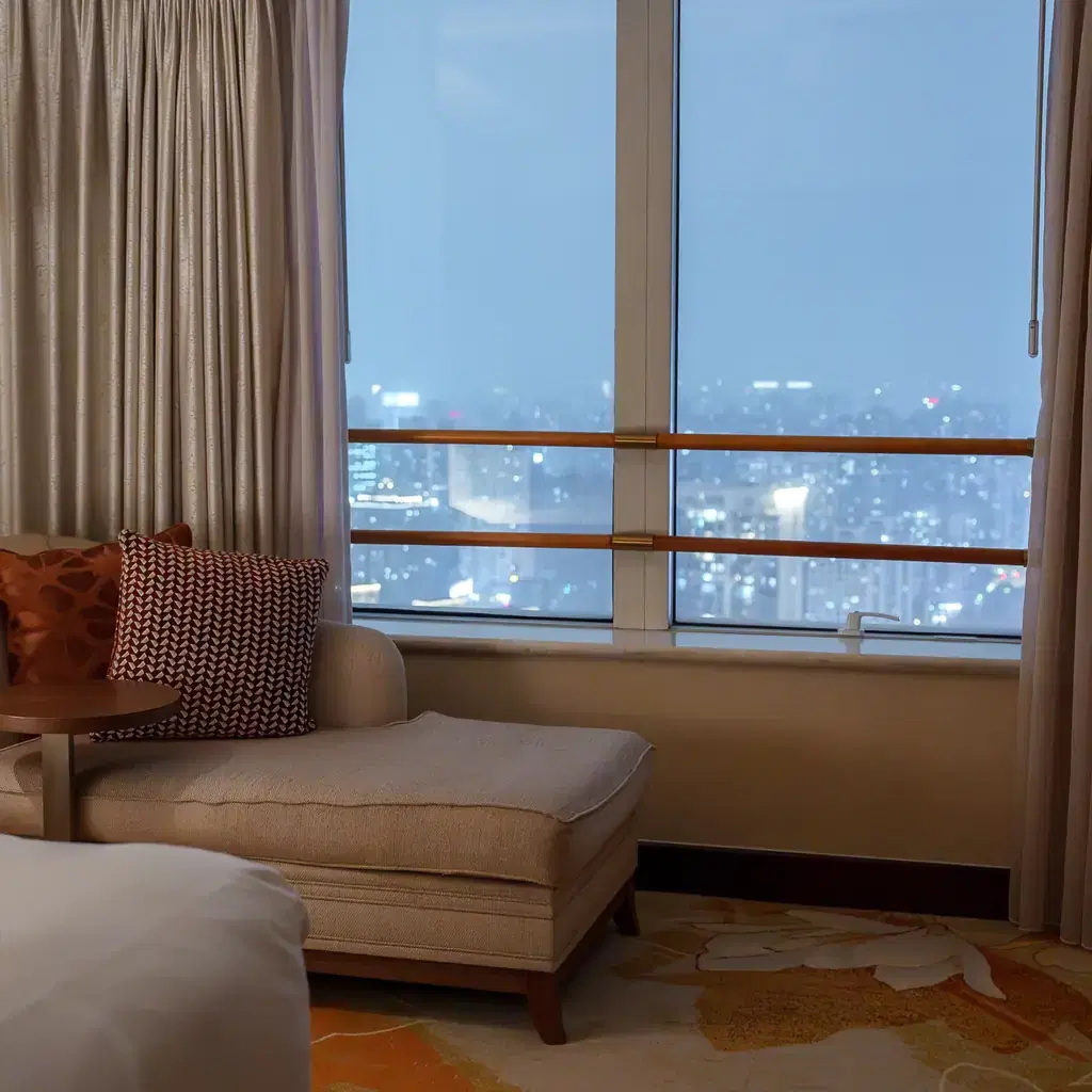 A chaise lounge beside a window with a city skyline visible at dusk, illustrating a separate floor-level rate.